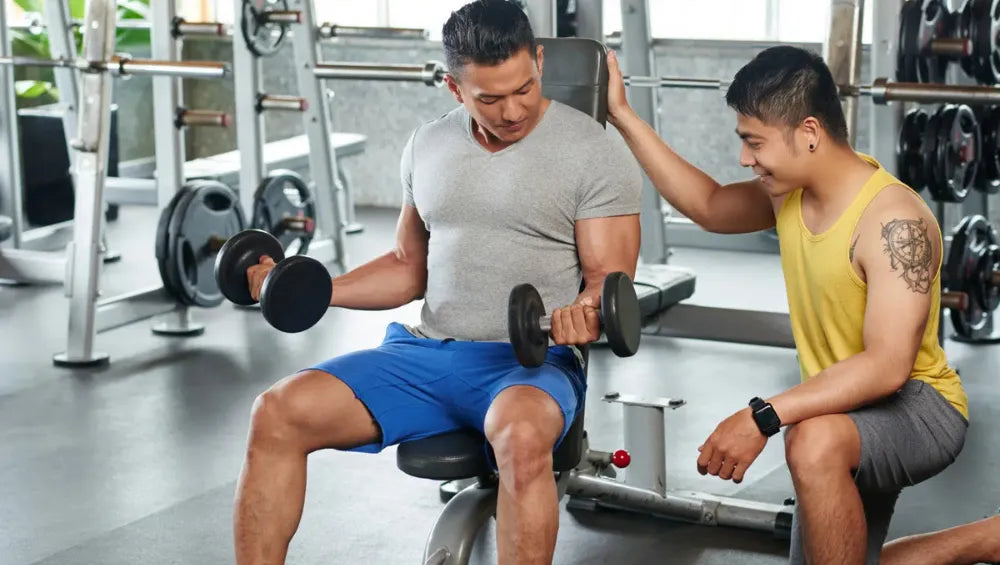 Homme assis sur un banc de musculation entrain de s'entrainer avec son coach.