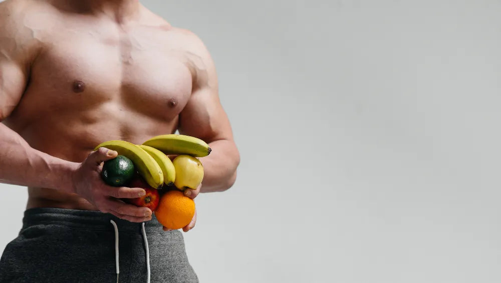 Homme musclé et sec torse nue tenant des fruits dans sa main sur un fond gris 