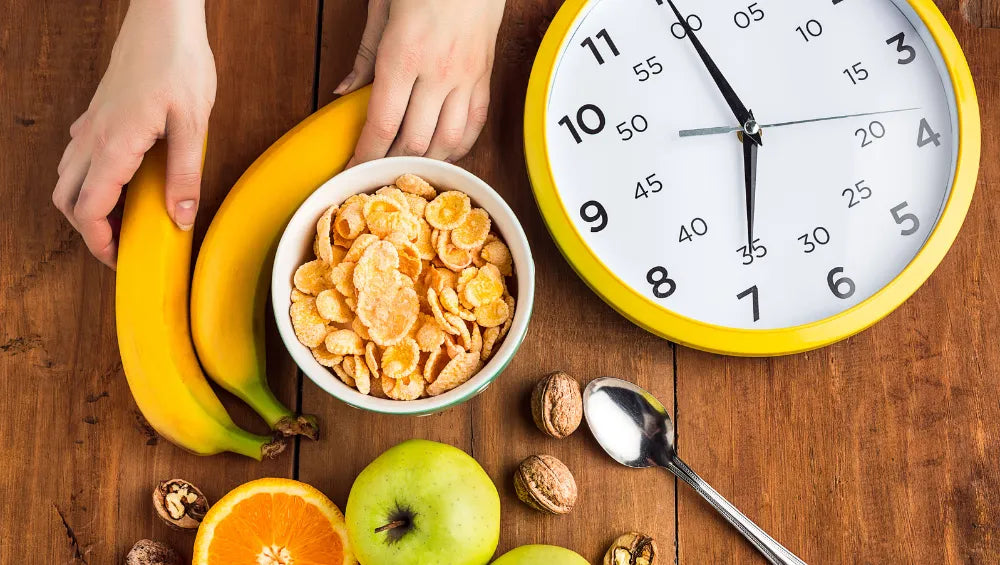 Table en bois garnis de corn flakes, bananes, pomme, noix et orange a coté d'une horloge avec un contour jaune