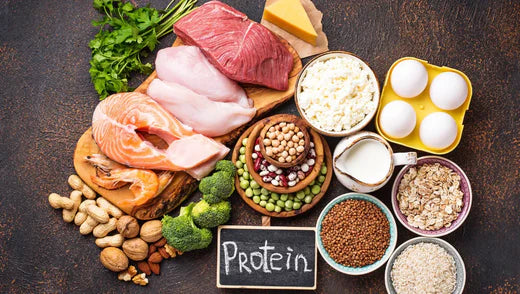 Table garnit de plusieurs aliments ayant une forte sources de protéine avec une ardoise écrit dessus à la craie "protein"