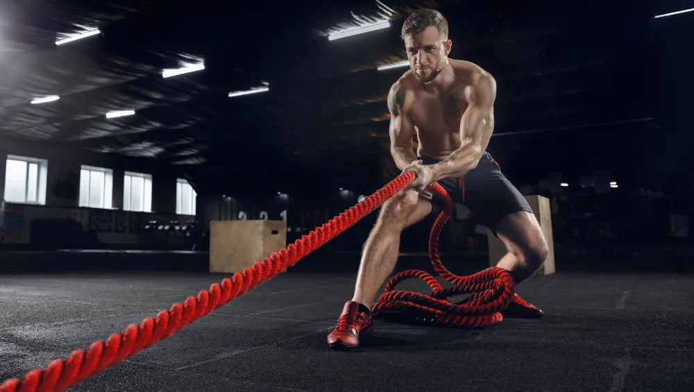 Homme torse nu musclé et sec dans une salle de crossfit en train de tirer sur une corde rouge