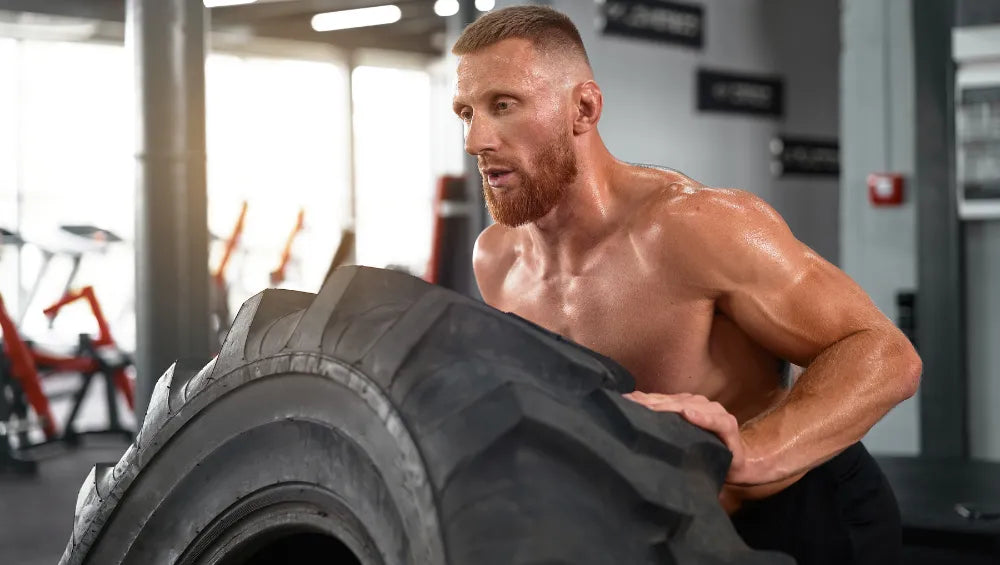 Homme musclé torse nu en train de retourner un pneu de camion dans une salle de sport