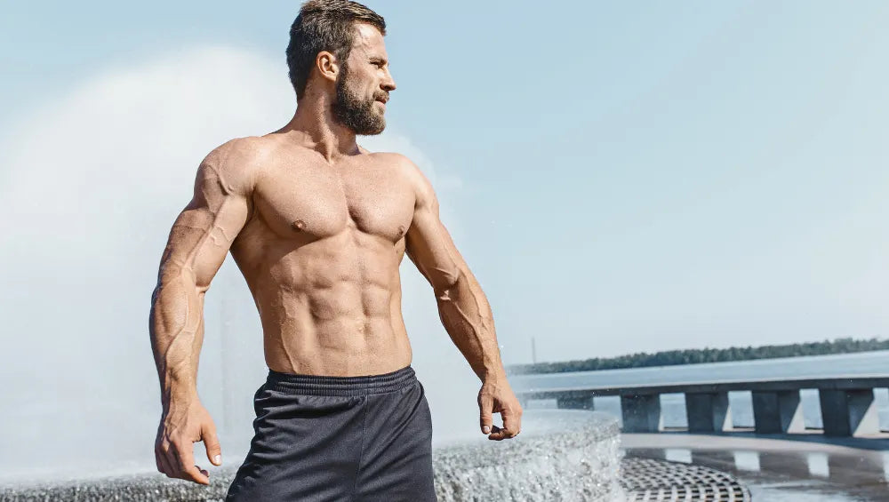 Homme musclé et sec torse nu devant une fontaine dehors en pleine air regardant à l'horizon