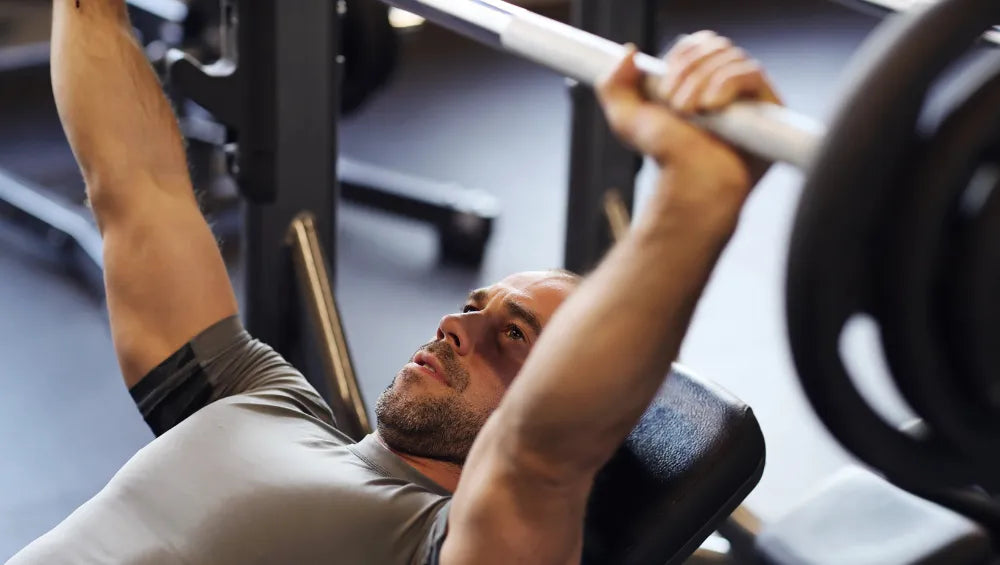 Homme en t-shirt gris en train d'effectué une série de développer couché incliné à la barre dans une salle de sport