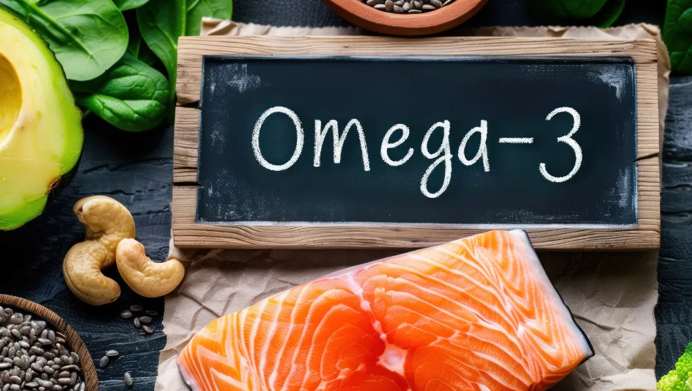 Ardoise avec écrit à la craie "omega-3" posé sur une table garnis de plusieurs aliments riche en omega 3 dont le saumon, les noix de cajou, avocat