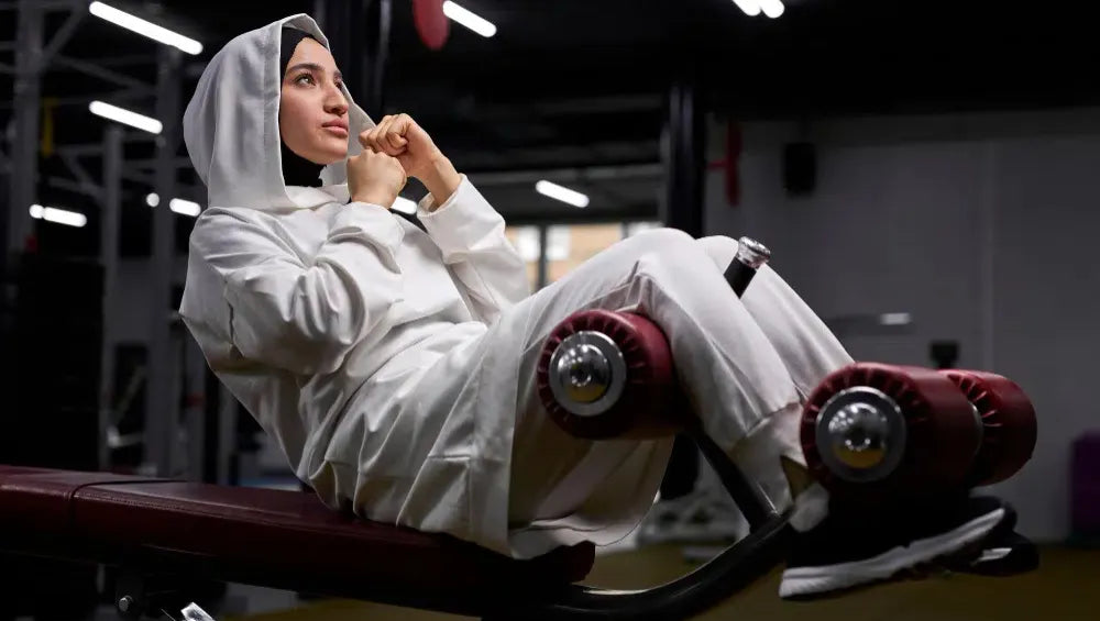 Femme voilé en pull et jogging blanc sur un banc à abdos 