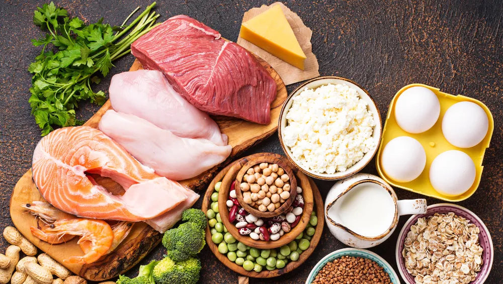 Une table garnis d'aliment, poisson, viande blanche et rouge, oeufs ainsi que du fromage quelques légumes verts et quelques céréales