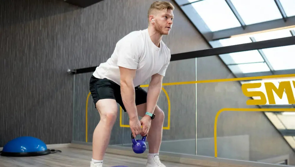 Homme flechis dans une salle de sport tenant entre ses deux main un Kettlebell exécutant un mouvement d'exercice