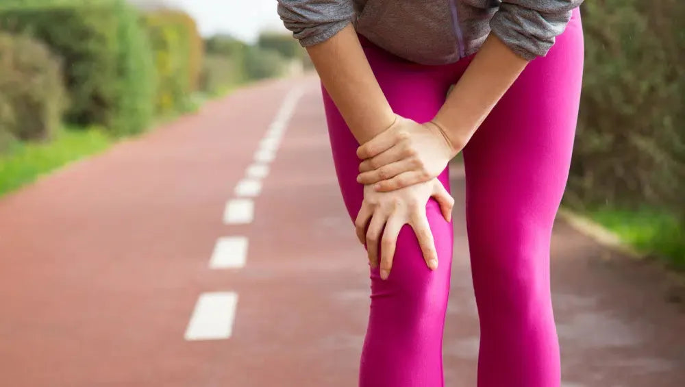 Femme fléchie ce tenant la jambe sur une piste de course 