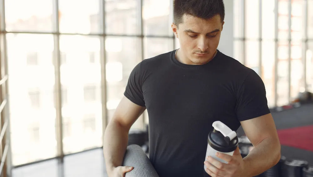 Homme en T-Shirt noir en train de regarder un shaker dans une salle de sport 