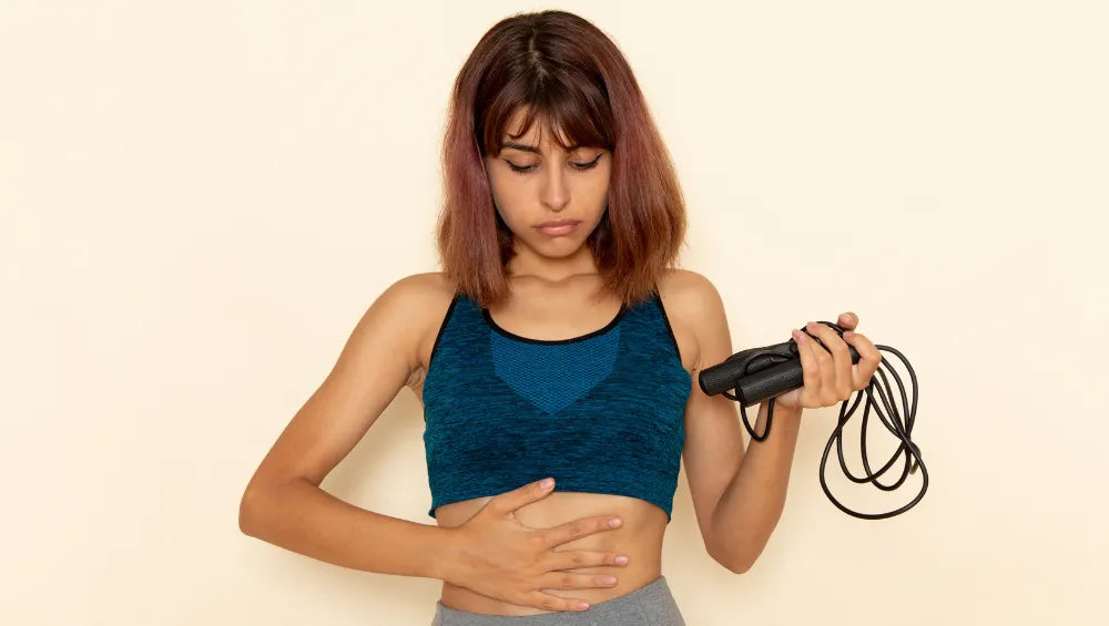 Femme en crop top bleu tenant une corde à sauter à la main et ce tenant le ventre de l'autre main